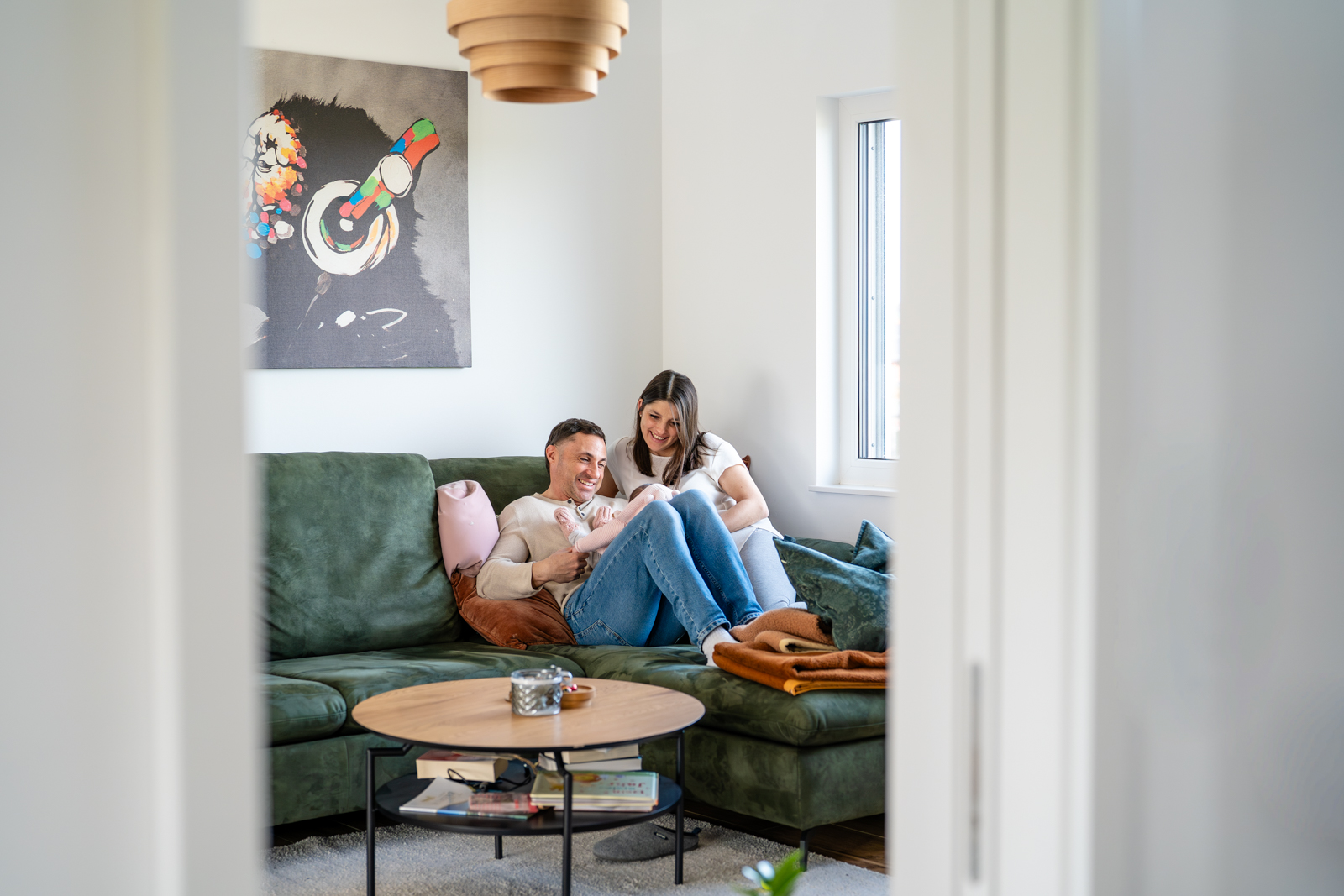 Frisch gebackene Eltern sitzen auf der Couch und halten ihr Neugeborenes
